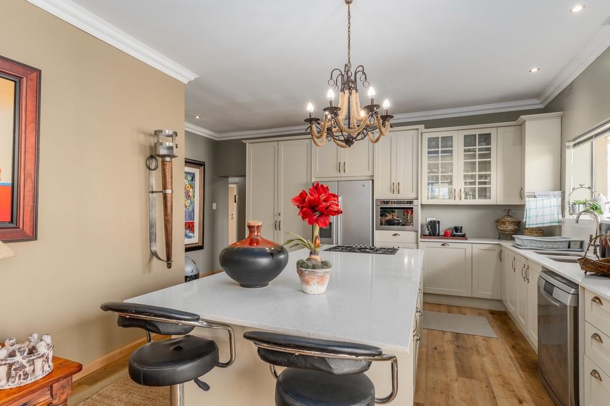 A well-appointed kitchen featuring a central island with stone countertops, shaker-style cabinetry, integrated appliances, and a decorative chandelier.