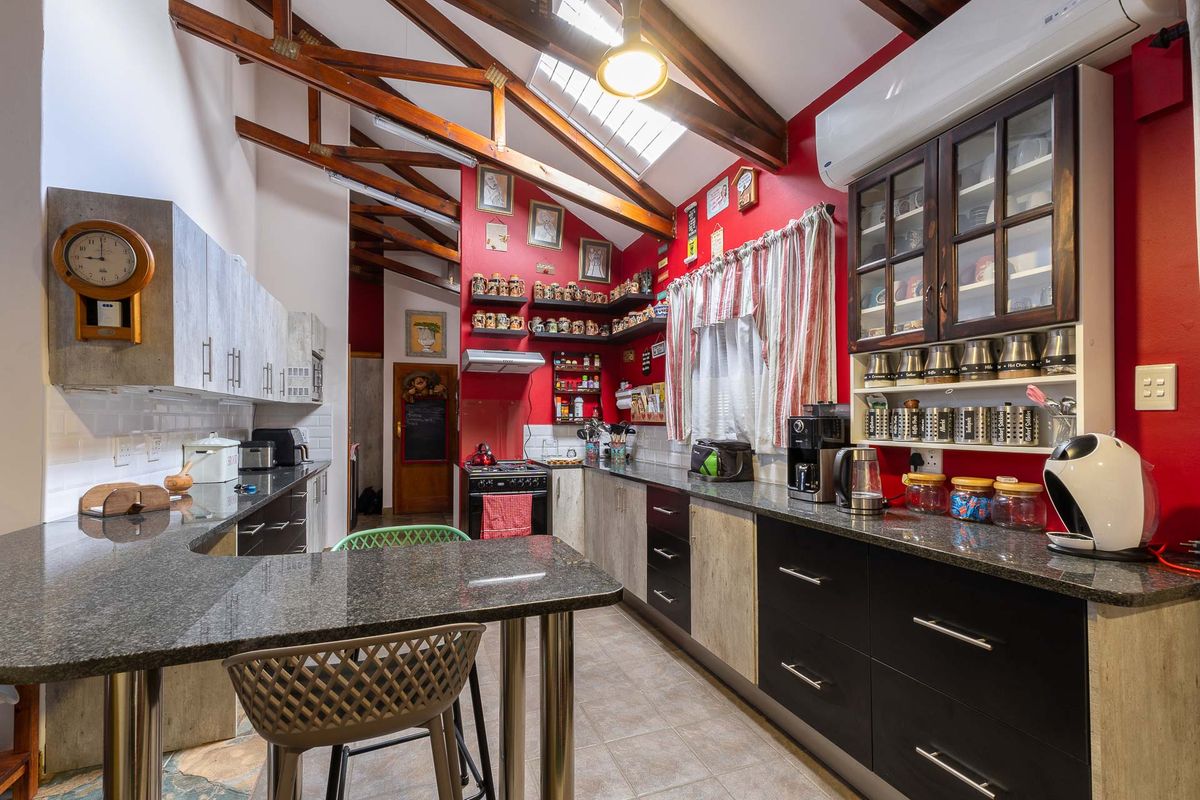 A spacious kitchen featuring exposed timber roof trusses, granite countertops, built-in cabinetry, and a breakfast bar area with tiled flooring.