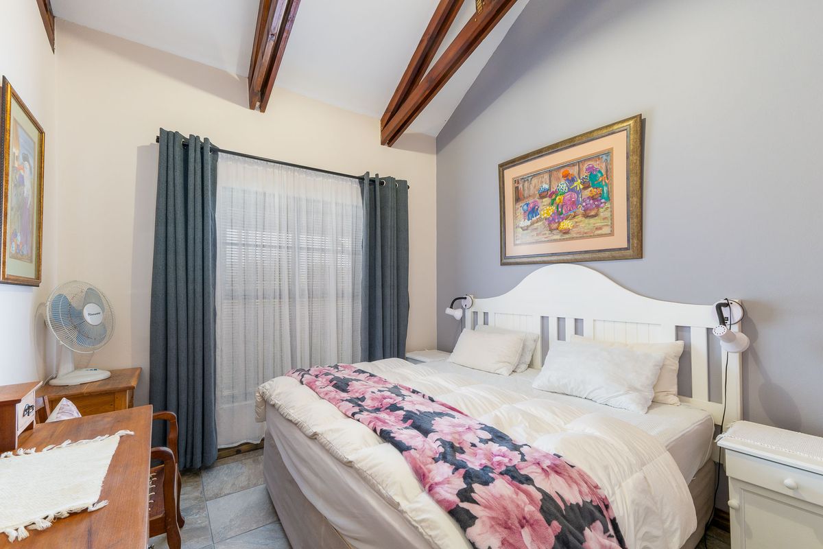 A cozy bedroom featuring vaulted ceilings with exposed timber beams, tiled flooring, and a large window with curtains.