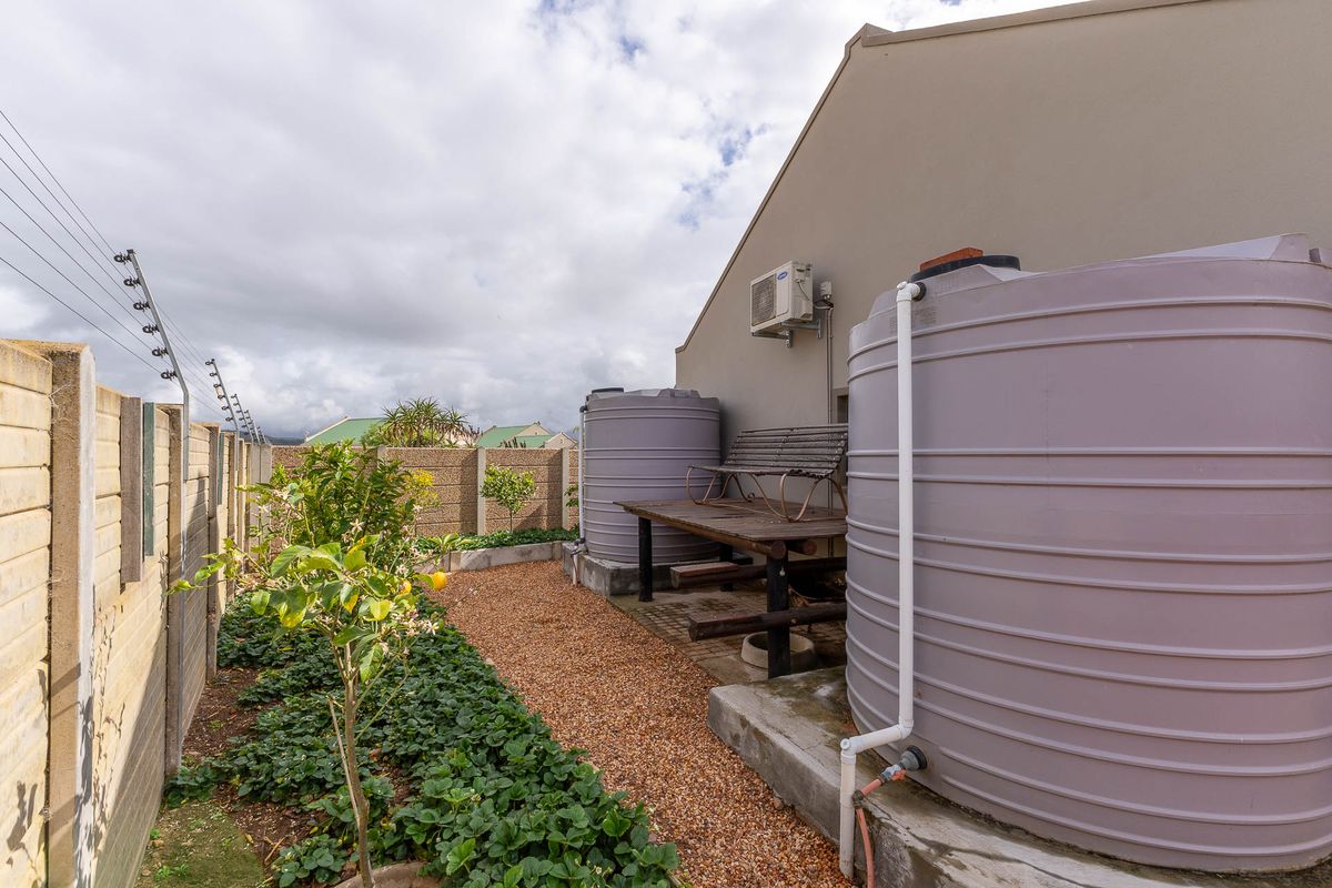 Side garden area featuring two large water storage tanks, gravel ground cover, and perimeter walling with electric fencing.