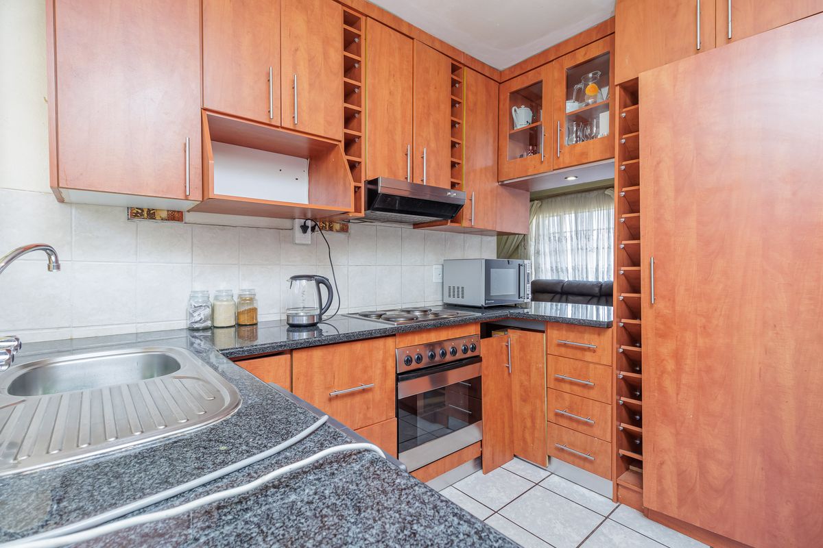 A functional kitchen featuring granite countertops, built-in oven, electric hob, extractor fan, and ample wooden cabinetry with integrated wine storage.