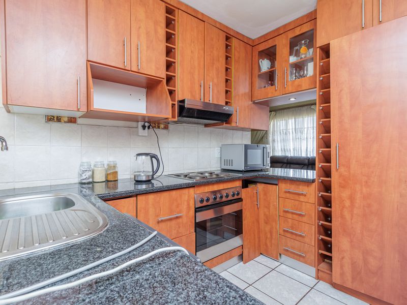 A functional kitchen featuring granite countertops, built-in oven, electric hob, extractor fan, and ample wooden cabinetry with integrated wine storage.