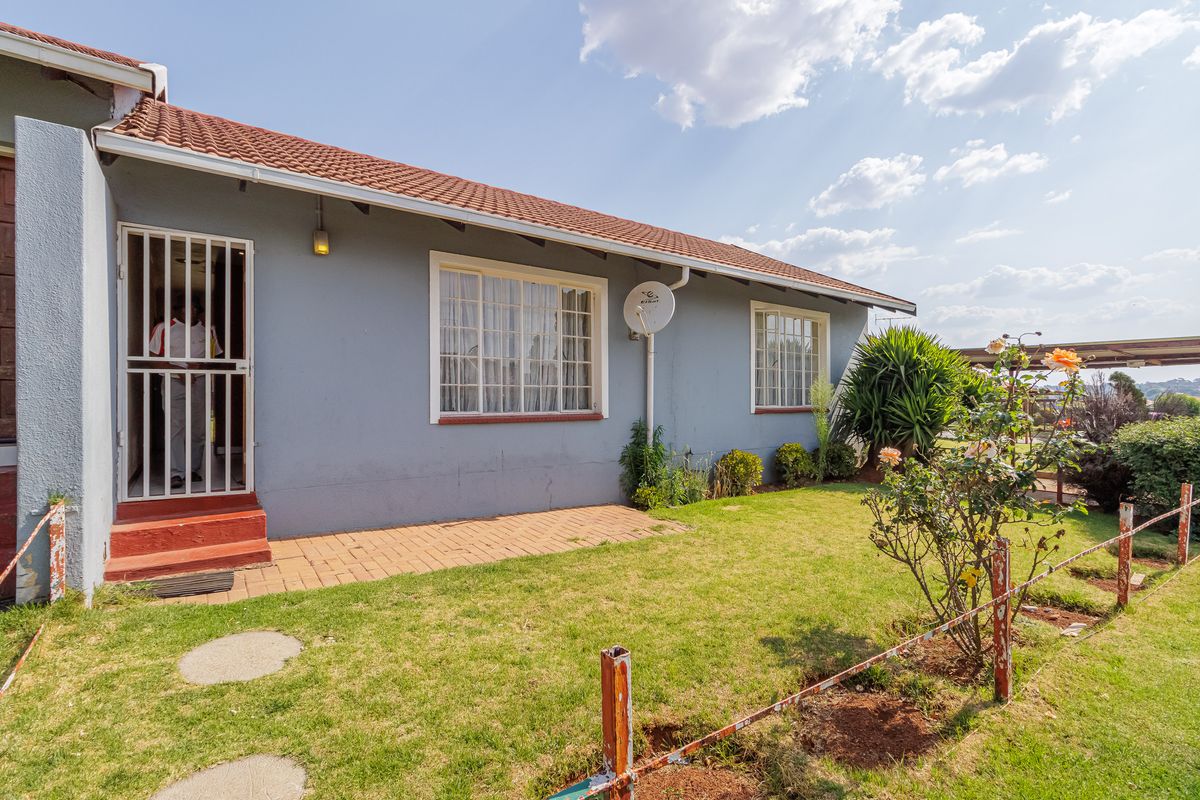 Rear exterior view of the townhouse featuring a small garden, brick paved area, and secure entrance with a metal security gate.