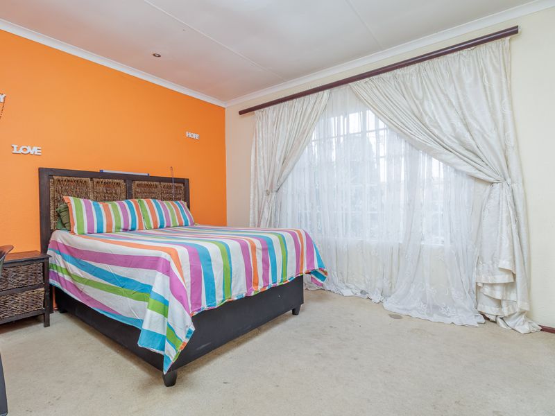 A bedroom featuring built-in cupboards, carpeted flooring, and a large window with curtaining.