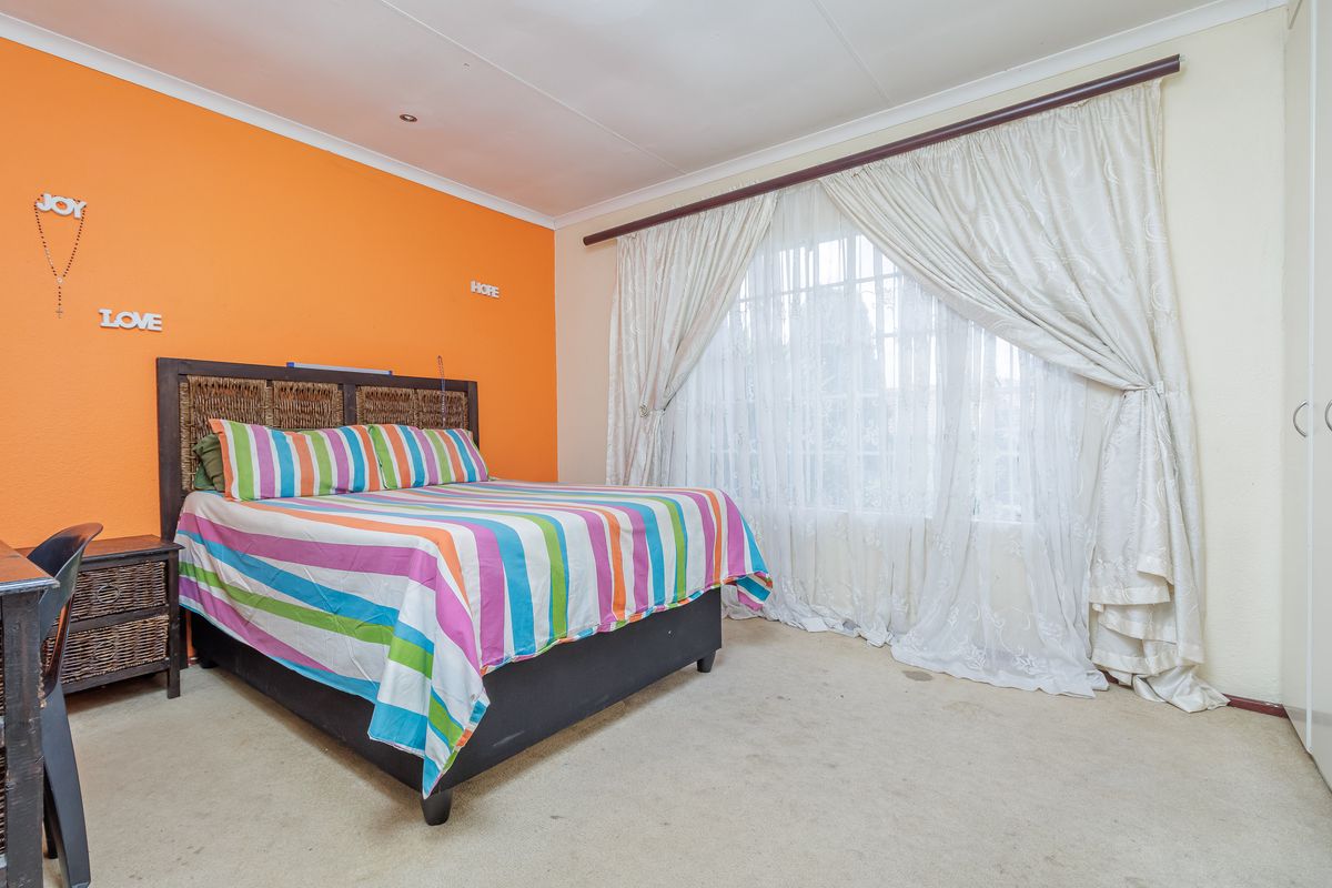 A bedroom featuring built-in cupboards, carpeted flooring, and a large window with curtaining.