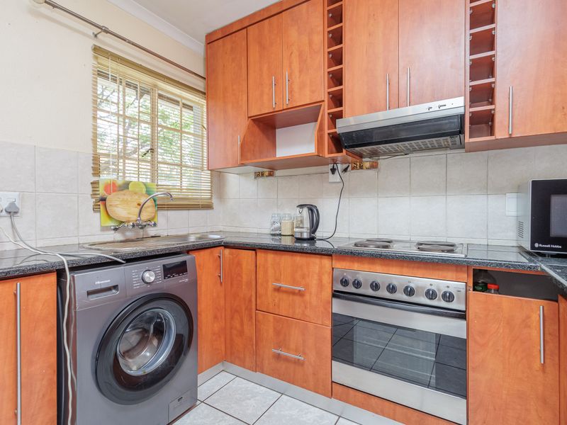 Functional kitchen featuring wood-finish cabinetry, granite countertops, built-in oven with hob, extractor fan, and tiled backsplash with integrated laundry plumbing.