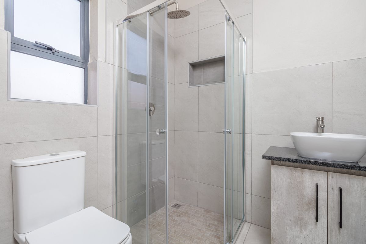 Modern bathroom featuring a glass-enclosed shower with a built-in niche, a contemporary vessel sink on a vanity, and a toilet.