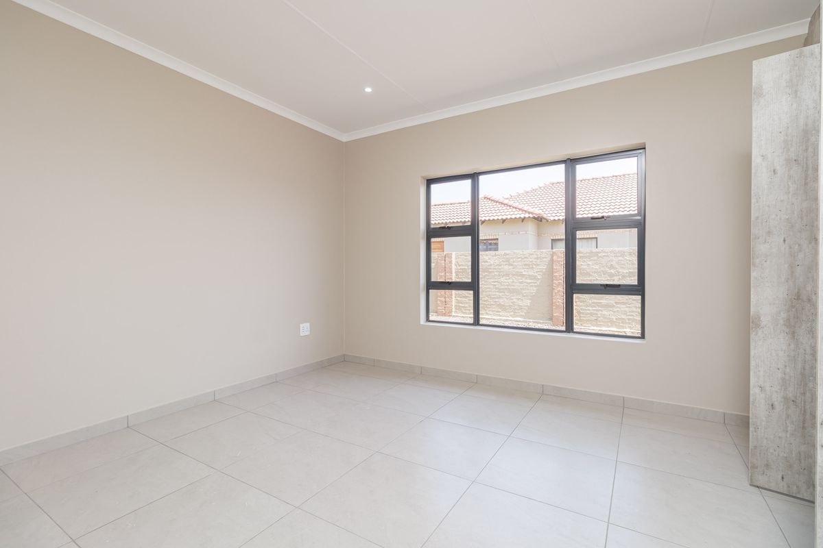 A bright, modern bedroom featuring neutral tiled flooring, clean painted walls, and a large window with dark frames.