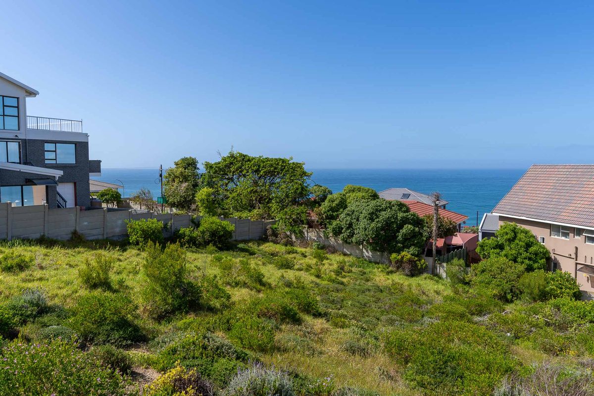 A vacant residential plot featuring natural vegetation and an elevated position with scenic ocean views, situated in a developed coastal neighborhood.
