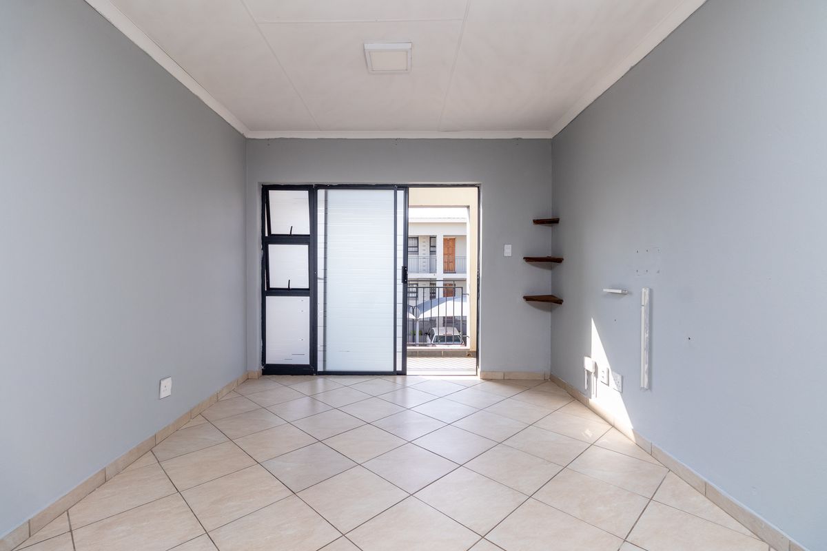 A bright, empty living room featuring neutral tiled flooring, grey walls, and a sliding glass door leading to an outdoor balcony area.