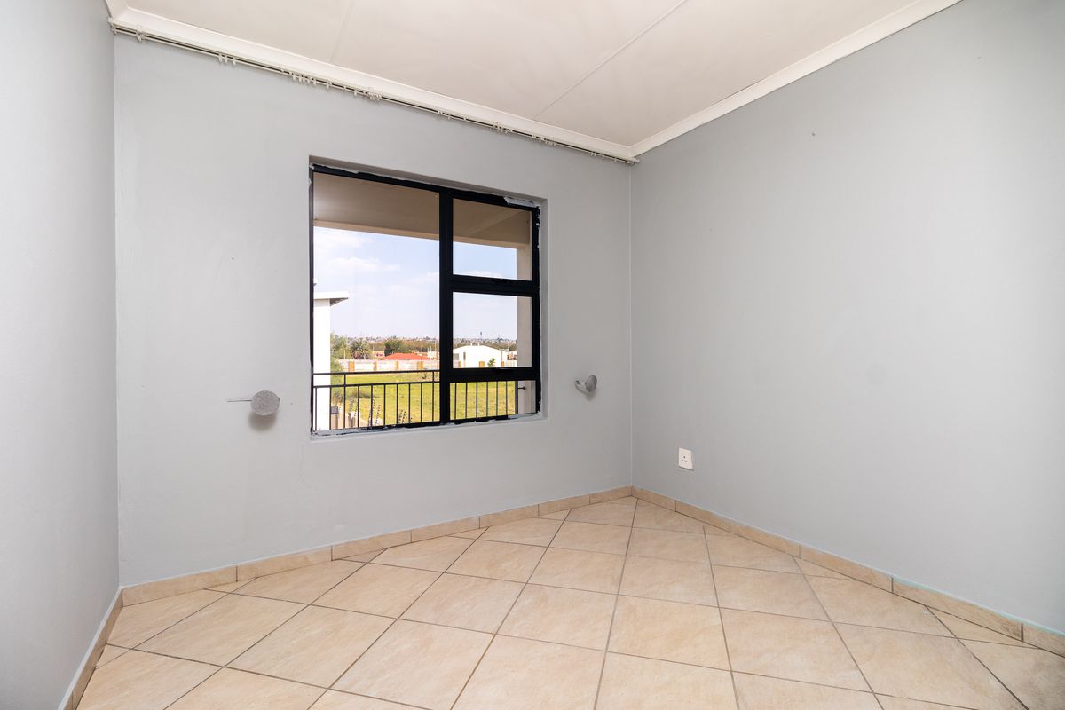 A bright, empty bedroom featuring neutral tiled flooring, light grey walls, and a large window with black framing.