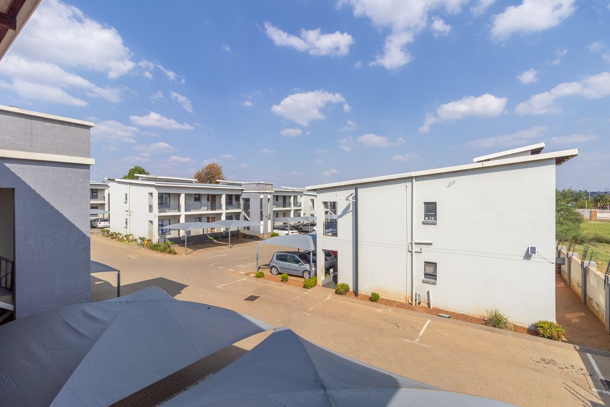 An elevated view of the apartment complex grounds, featuring paved parking areas with shade-cloth carports and multi-story residential building blocks.
