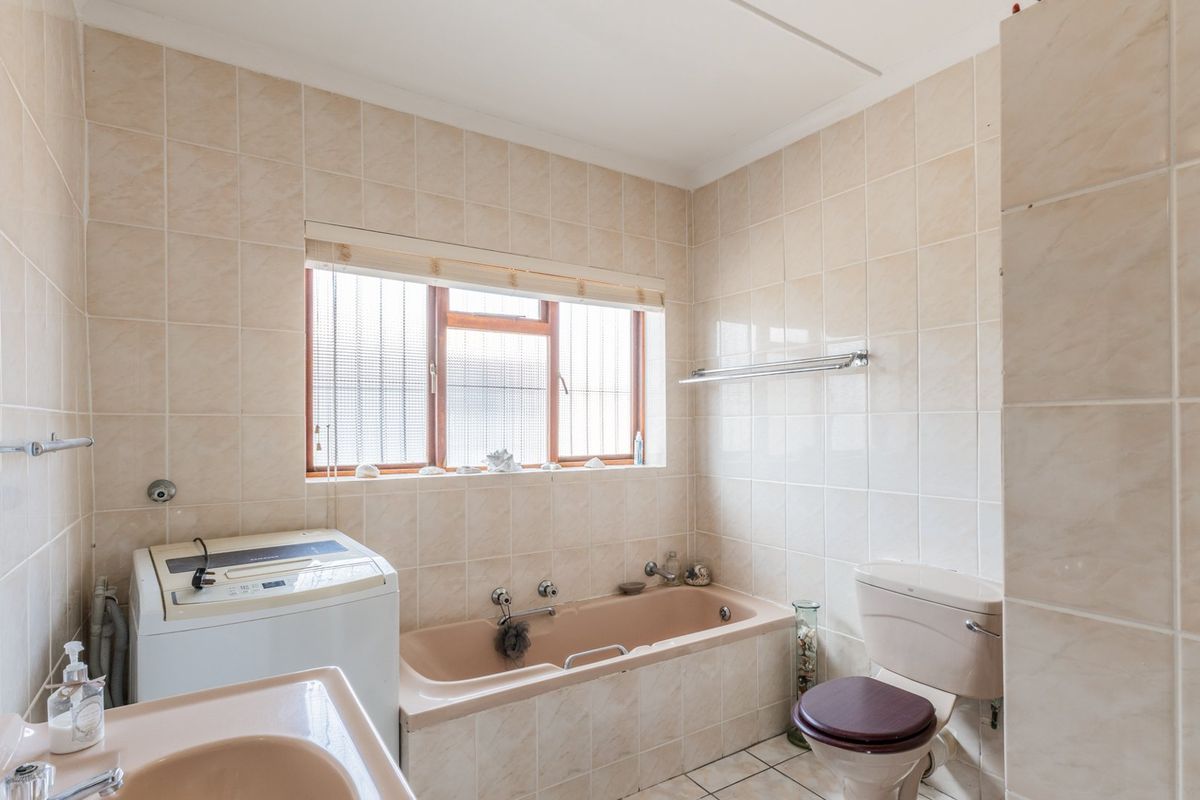 A dated bathroom featuring a peach-toned bathtub and basin, tiled walls, and a window with security bars.