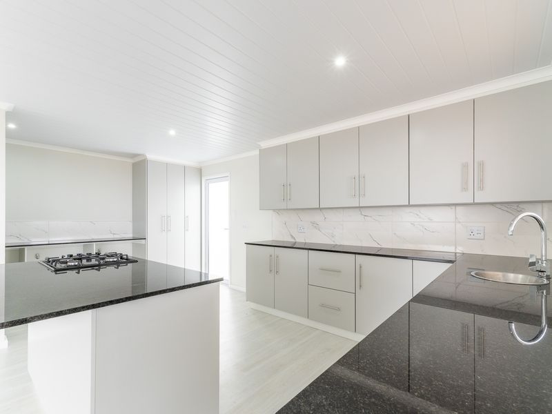 Modern kitchen featuring light grey cabinetry, contrasting black granite countertops, marble-look splashbacks, and a central island with a built-in gas hob.