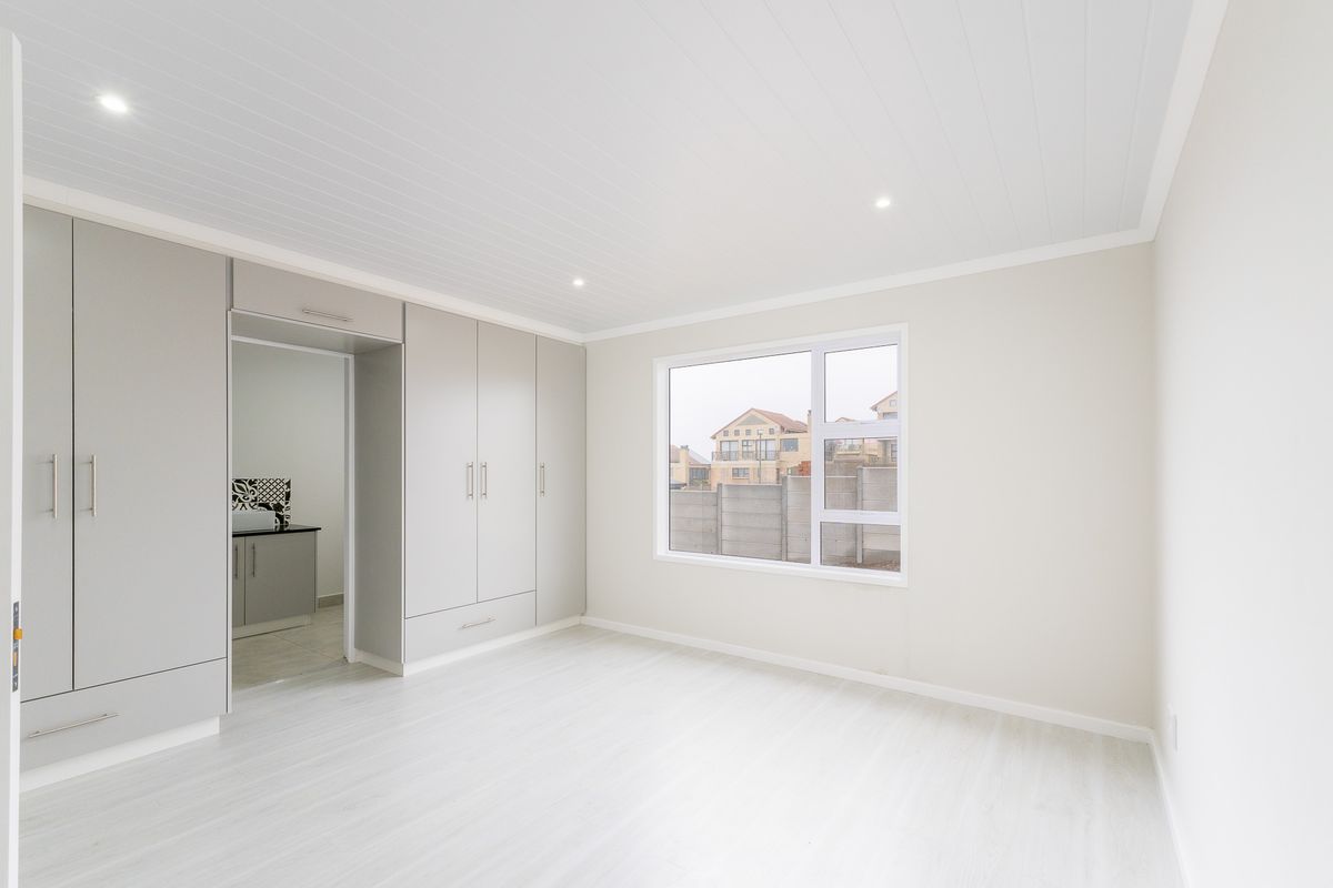 A bright, modern bedroom featuring neutral tones, built-in cabinetry, recessed ceiling lighting, and light-colored flooring, offering a clean and contemporary living space.