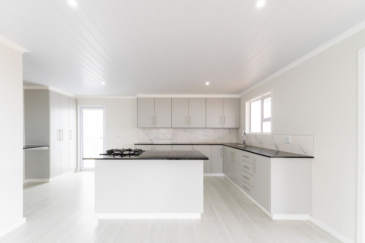 Modern kitchen featuring light grey cabinetry, dark stone countertops, a central island with a built-in gas hob, and marble-look splashbacks.