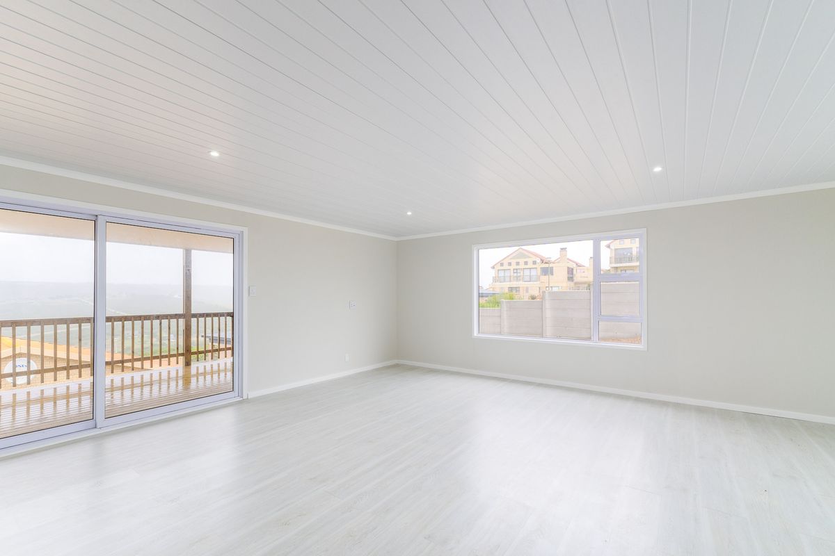A bright, spacious, and empty living area featuring light-toned laminate flooring, a modern tongue-and-groove ceiling, and large windows with access to a balcony.