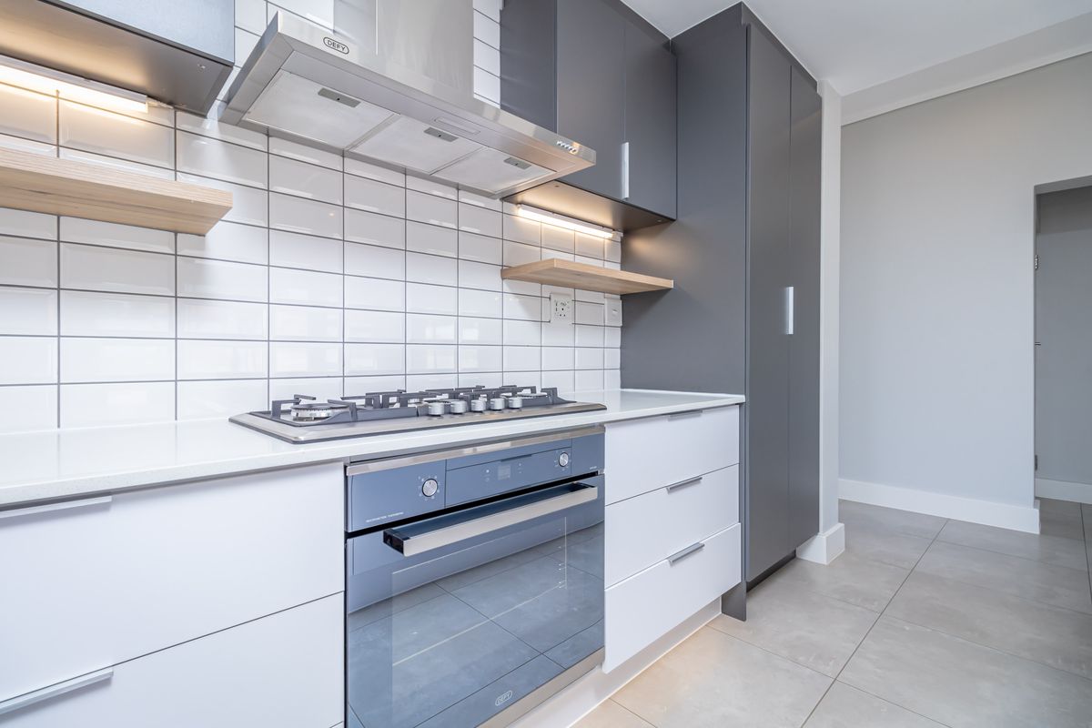 Modern kitchen featuring sleek grey and white cabinetry, subway tile backsplash, built-in gas hob, extractor fan, and integrated oven with stone countertops.