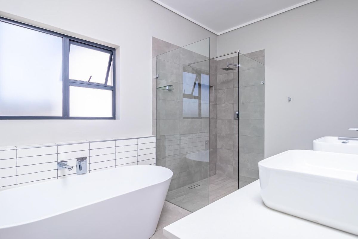 Modern bathroom featuring a freestanding bathtub, a glass-enclosed walk-in shower with grey tiling, and double vanity basins.
