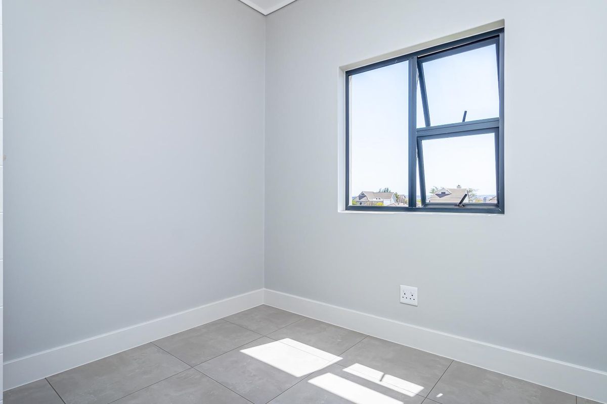 A bright, empty bedroom featuring neutral grey walls, modern tiled flooring, and a large window with dark frames.