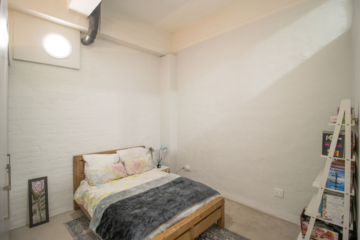 A bedroom featuring industrial-style exposed piping, painted brick walls, and polished concrete flooring.