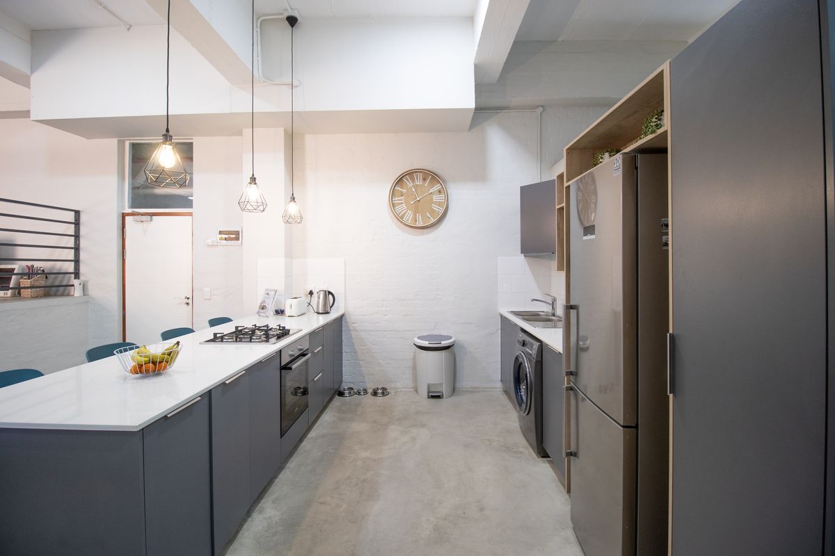 Modern open-plan kitchen featuring sleek grey cabinetry, stone countertops, integrated gas hob, built-in oven, and polished concrete flooring in a contemporary industrial style.