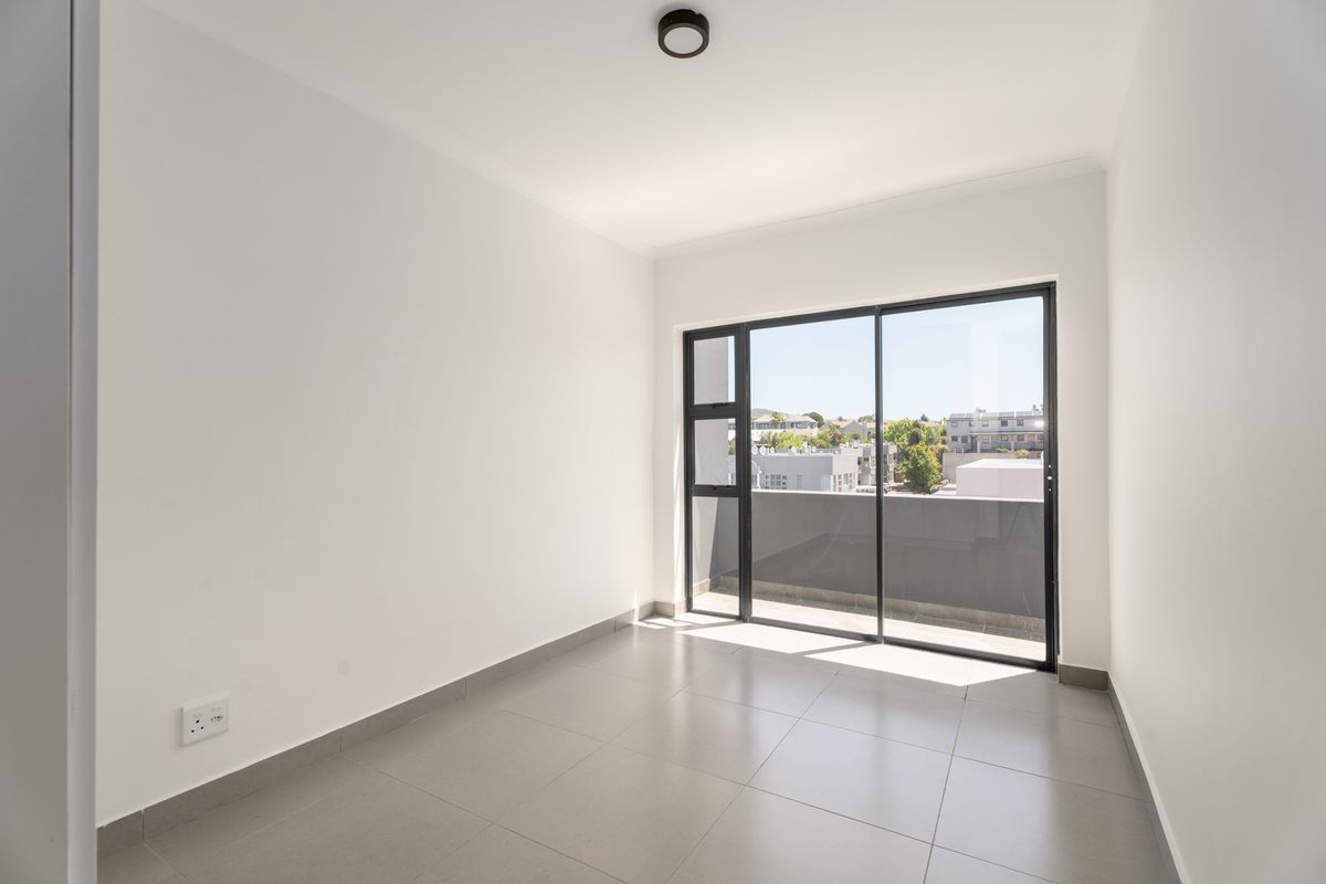 A bright, empty bedroom featuring neutral tiled flooring, a modern ceiling light, and a large sliding glass door providing access to an outdoor balcony.