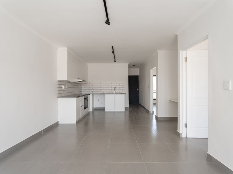 A bright, modern open-plan living and kitchen area featuring neutral tiled floors, white cabinetry, subway tile backsplash, and contemporary track lighting.