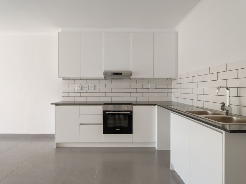 Modern kitchen featuring white cabinetry, subway tile backsplash, granite countertops, built-in oven, extractor fan, and stainless steel sink with grey floor tiles.