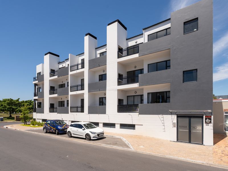 Modern multi-story apartment building facade featuring a contemporary white and grey exterior, private balconies with metal railings, and a paved ground-level entrance.