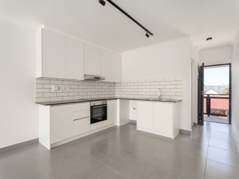 Modern kitchen featuring white cabinetry, subway tile backsplash, integrated oven, extractor fan, and sleek grey floor tiles with direct access to a balcony.