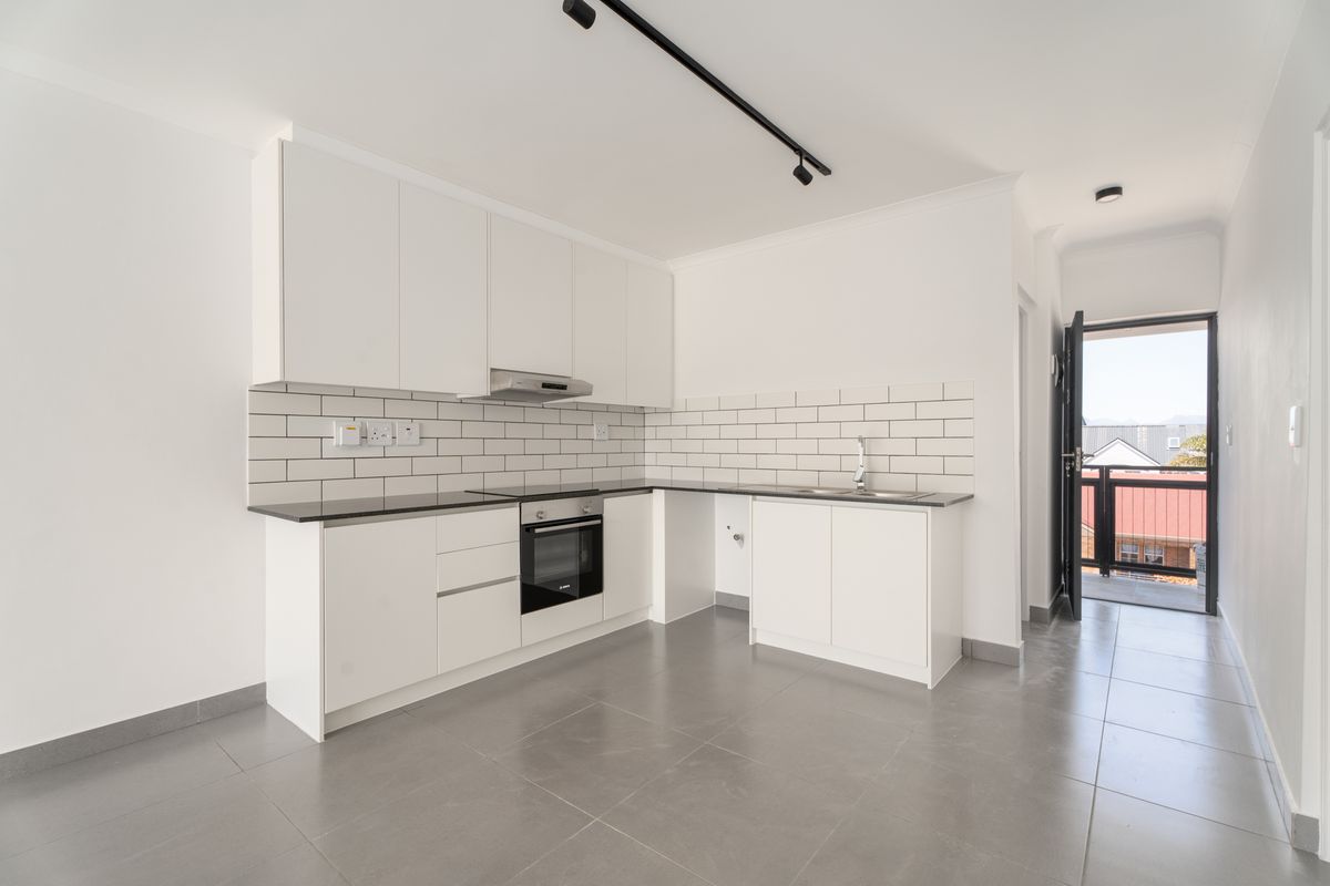 Modern kitchen featuring white cabinetry, subway tile backsplash, integrated oven, extractor fan, and sleek grey floor tiles with direct access to a balcony.