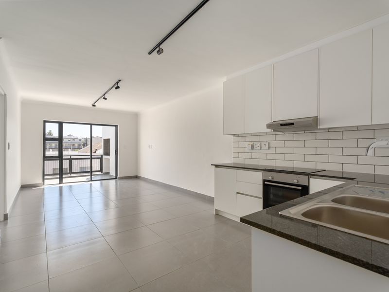 Modern open-plan living area featuring a sleek kitchen with stone countertops, subway tile backsplash, and direct access to a private balcony.