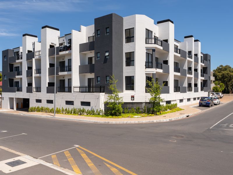 Modern multi-story apartment complex featuring a contemporary white and charcoal facade with private balconies and integrated ground-level parking access.