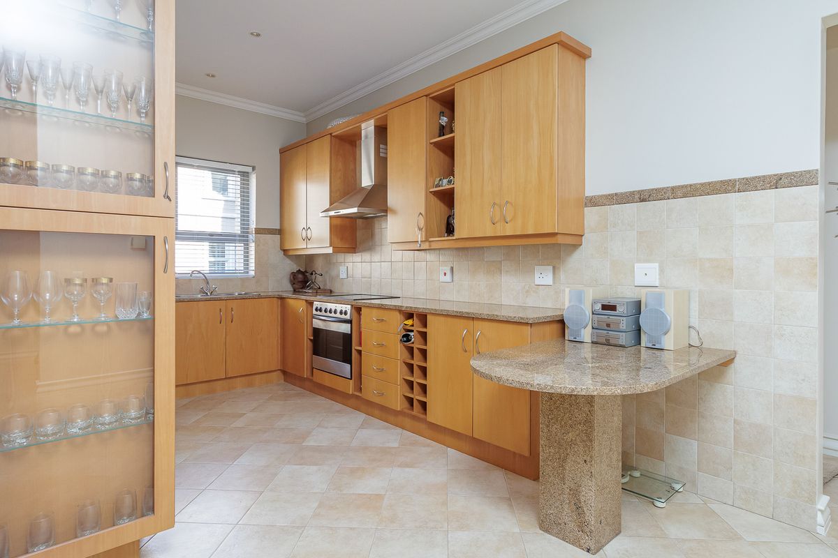 A functional kitchen featuring light wood cabinetry, granite countertops, a built-in oven with extractor fan, and tiled flooring.