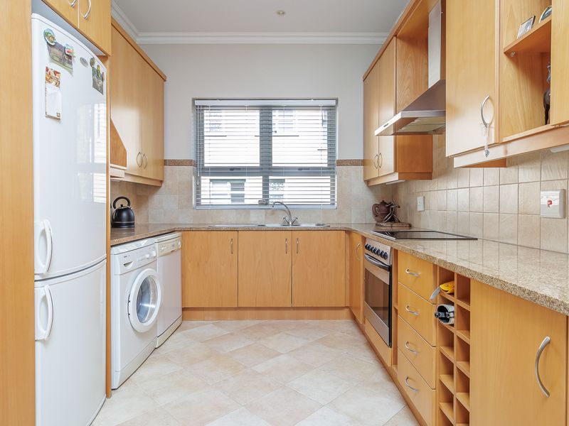 A functional galley-style kitchen featuring light wood cabinetry, granite countertops, tiled backsplash, and integrated stainless steel oven and extractor fan.