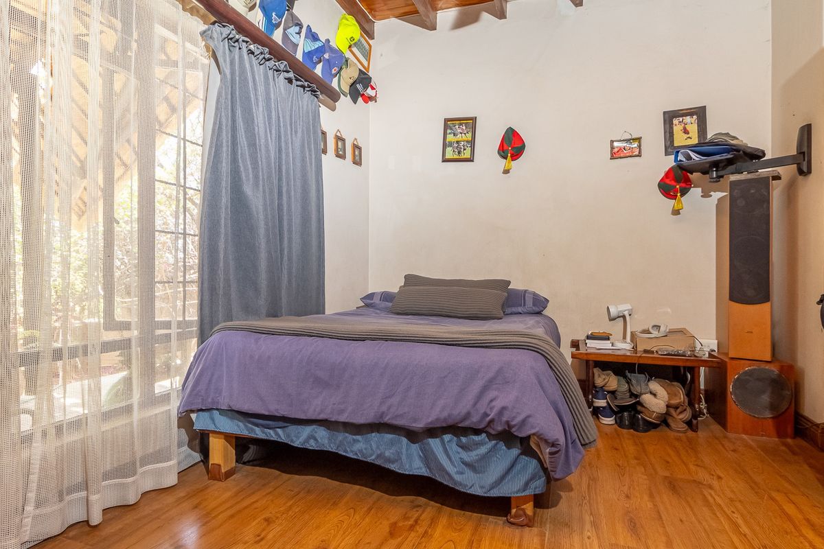 A bedroom featuring timber flooring, exposed wooden ceiling beams, and a large window with access to an outdoor area.