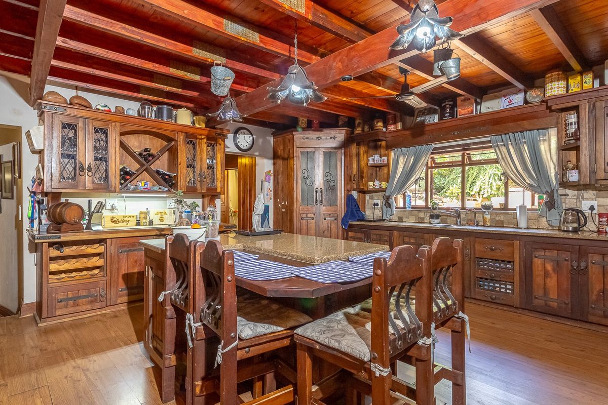 A rustic kitchen featuring extensive timber cabinetry, exposed wooden ceiling beams, a central island with stone countertop, and integrated storage solutions.