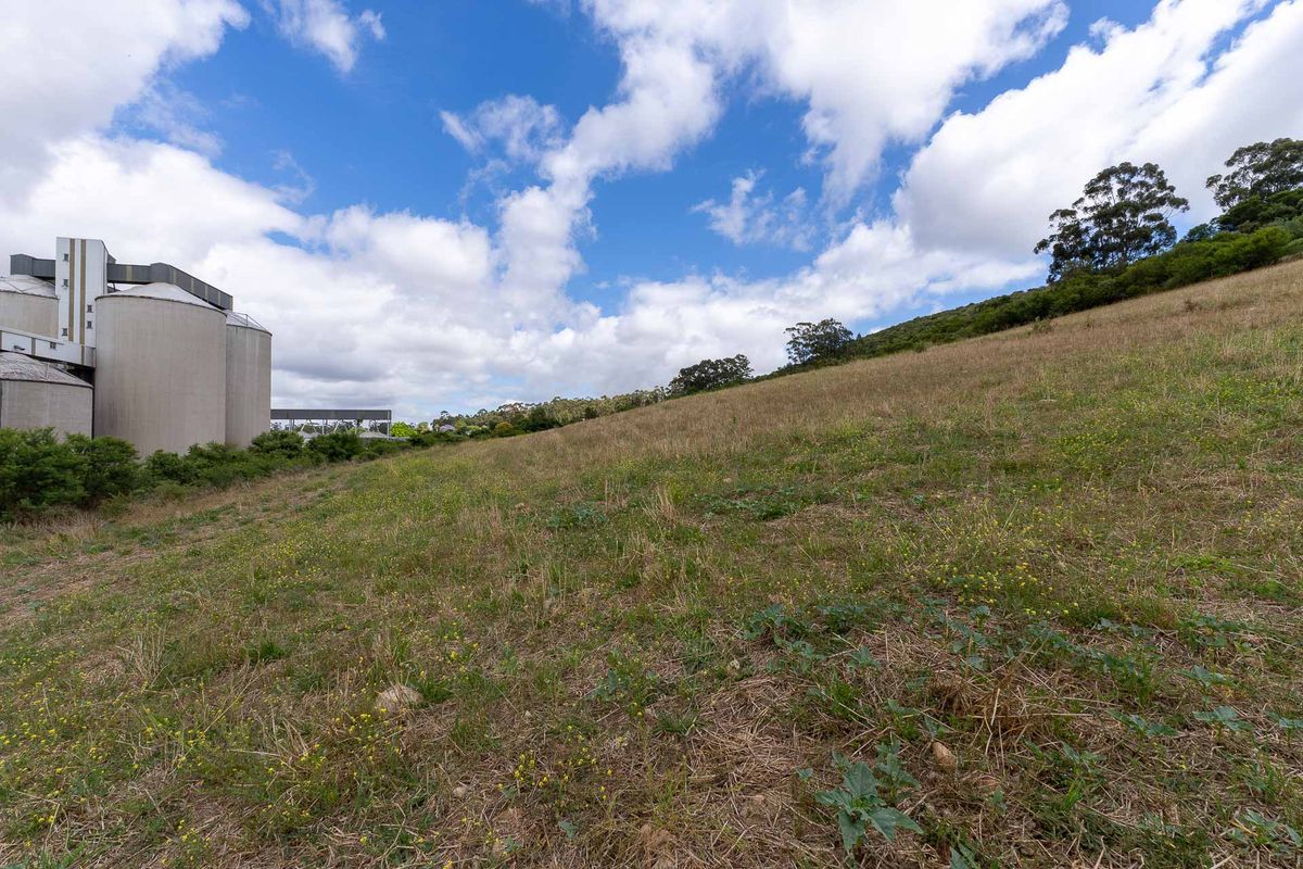 A view of the vacant residential land featuring a sloping grassy terrain with nearby industrial silo structures in the background.