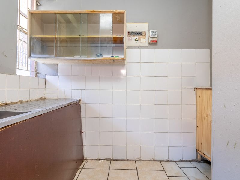 A dated kitchen area featuring a stainless steel sink, tiled splashback, and wall-mounted cabinetry, requiring renovation to modernize the space.
