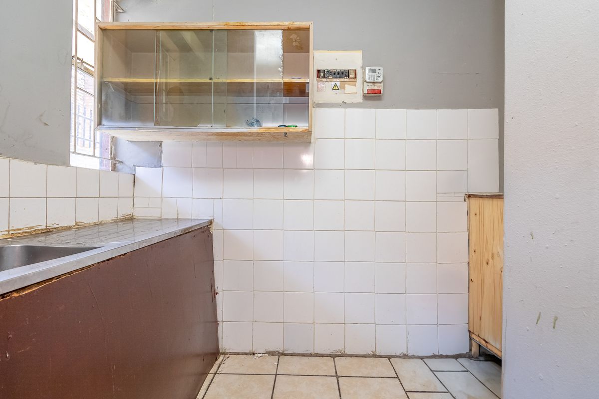 A dated kitchen area featuring a stainless steel sink, tiled splashback, and wall-mounted cabinetry, requiring renovation to modernize the space.