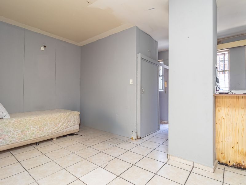 Open plan living area featuring tiled flooring, a breakfast bar, and security bars on windows, requiring cosmetic updates to the walls and ceiling.