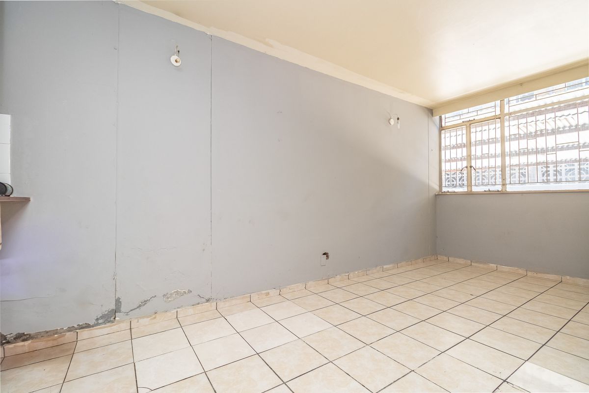 An empty living area featuring tiled flooring and a window with security bars, requiring cosmetic attention to the walls and finishes.