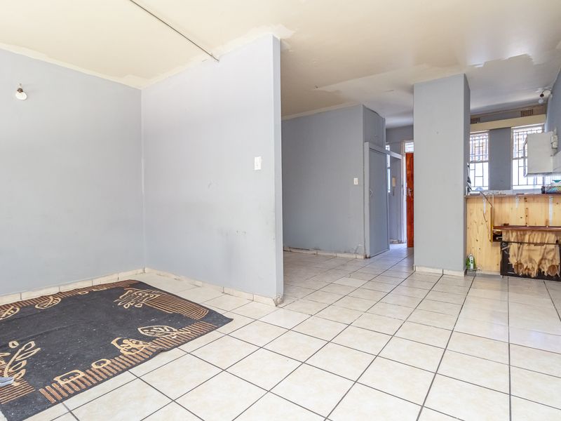 Open plan living and kitchen area featuring tiled flooring and basic built-in cabinetry, requiring cosmetic updates and ceiling finishing.