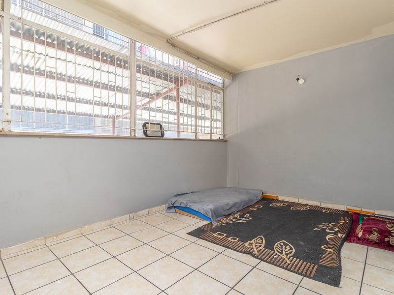 A vacant bedroom featuring tiled flooring and a large window with security bars, requiring minor cosmetic repairs to the ceiling and walls.