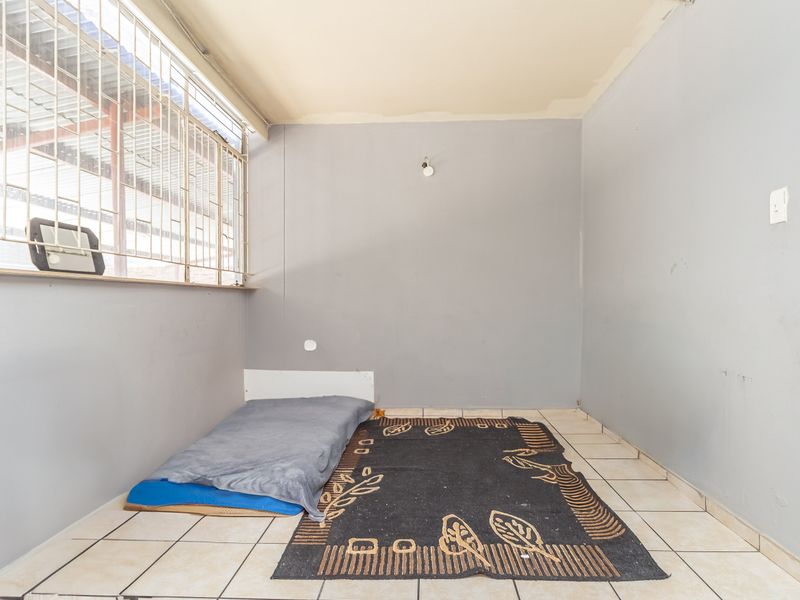 A simple bedroom featuring tiled flooring and security bars on the window, presenting a blank canvas for potential renovation or staging.
