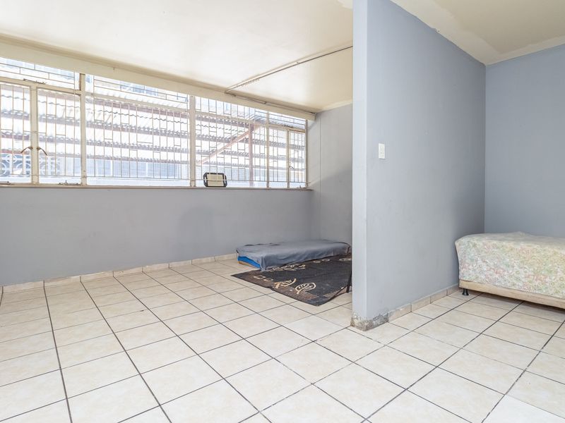 A bedroom space featuring tiled flooring, a partition wall, and large windows with security bars, requiring cosmetic updates to improve its overall condition.