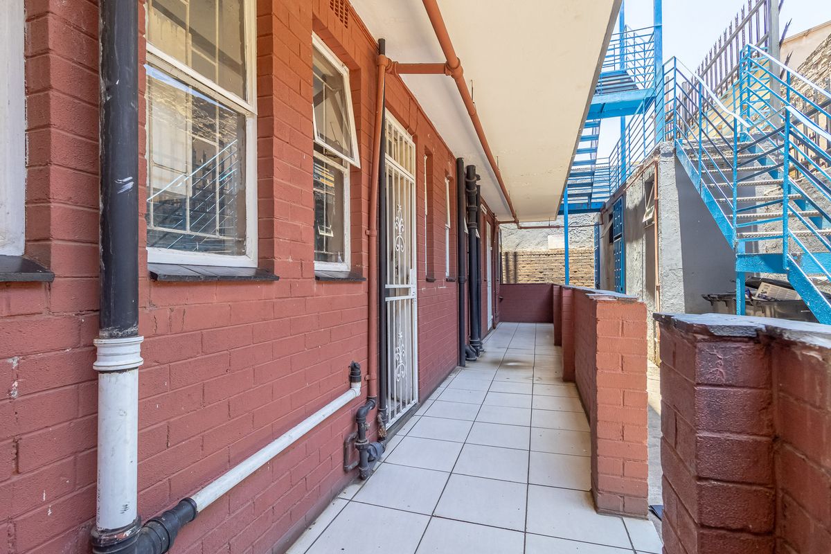 A rear exterior walkway featuring red brick walls, tiled flooring, and external metal stair access to the apartment building.