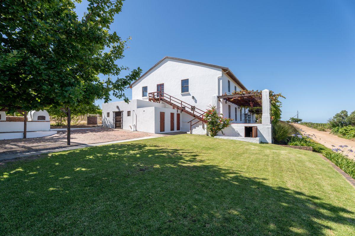 A rear view of the farmhouse featuring a white exterior, external staircase, pergola-covered patio area, and well-maintained lawn.
