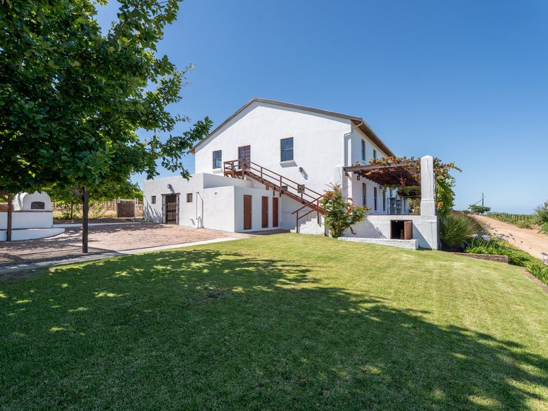 A rear view of the farmhouse featuring a white exterior, external staircase, pergola-covered patio area, and well-maintained lawn.